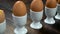 Row of boiled eggs in egg cups on a wooden table to toast soldier being dipped in the yolk of a broken open egg