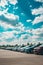 Row of cars parked in parking lot under cloudy blue sky. Generative AI