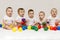 Row of caucasian babies sitting side by side looking away isolated on gray background. Five cute babies playing with