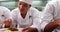 Row of chefs garnishing spaghetti dishes with basil leaf