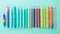 A row of colorful pencils and pens on pastel green color background.