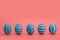 A row of five blue decorated Easter eggs on a pink background.