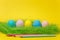Row of five colorful pastel monophonic painted Easter eggs, pencils in green grass on yellow background for card or