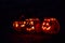 Row of four Jack O Lantern carved pumpkins illuminated with burning candle flames inside