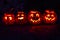 Row of four Jack O Lantern carved pumpkins illuminated with burning candle flames inside