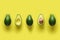 Row of fresh wholes and halves of organic avocado with kernels in center on yellow backgrond. Top view