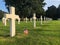 Row of gravestone crosses in cemetery with American flag.