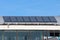 Row of large dark solar water heating panels mounted on top of old metal roof of local sports hall