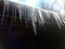 A row of long icicles hangs from the roof against the blue sky