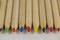 Row of long wooden pencils with colored cores close up on gray blurred background