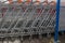 Row of metal shopping carts with orange handles standing tightly one in another outdoor in front of DIY store