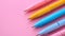 A row of multicolord pens on pastel pink background.