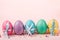 Row of multicolored decorated Easter eggs on pink background