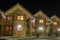 Row of new two-storied ecological wooden comfortable decorated cottages hotels on clean illuminated street under dark night sky.