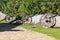 Row of old ancient vintage cannons on the green lawn against grey wooden palisade of the protective fence stakewall