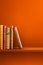 Row of old books on orange shelf. Vertical background