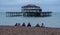 Row of people sitting on pebbly beach in Brighton UK on a wintry afternoon in December, in front of the ruins of West Pier.