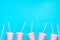 Row of pink empty paper cups striped drinking straws arranged in bottom border on blue background. Creative flat lay. Birthday