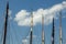 Row of sail boat mast tips and attached cables against a cloudy blue sky