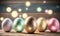 a row of shiny colored easter eggs on a wooden table with boke lights in the backgroup of the photo behind them