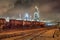 Row of train wagons with an illuminated oil refinery at night in Port of Antwerp, Belgium