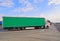 A row of trucks in a parking lot. In the foreground a truck with a semi-trailer. Green tarpaulin