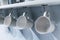 Row of white ceramic cups hanging on silver metal hook under white cabinet.