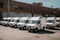 A row of white delivery trucks parked in a parking lot. Generative AI image.