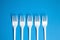 A row of white forks on blue background, top view. Disposable plastic tableware