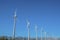 Row of windmills with three blades against blue sky on a sunny day.