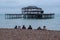 Row of women sitting on pebbly beach in Brighton UK on a wintry afternoon in December, in front of the ruins of West Pier.