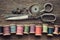 Row of wooden spools of multicolored threads, tailoring scissors, thimbles, measuring tape, sewing items on wooden board.
