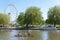 Rowing boat with three people on river with big ferris wheel and willow tree in the background