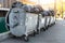 Rows of many big metal overloaded dumpster cans full of black plastic trash litter bags near residential building at