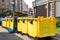 Rows of many big plastic yellow dumpster cans full of black plastic trash litter bags near residential building at city