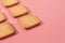 Rows of many whole square cookies lies on pink desk on kitchen