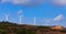 Rows of modern windmills in an energy wind farm on top of a hill against a blue sky