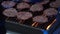 Rows of raw burger patties flipped on hot seared grill pan overhead.