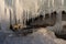 Rows of stalactite icicles hang from the stone. Icicles on the lake beach on the background of blue water. Fragments of