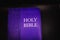 A royal blue, leather-bound printed copy of the King James version of the Holy Bible against a black backdrop