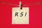 RSI Relative Strength Index text on a yellow sticker hanging on a rope with clothespins on a red background