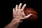 Rubber orange basketball ball is catch by a hand on a black background
