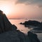 Rugged coastline at sunset with sun poking behind rock and creating rays