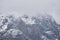 Rugged mountain landscape - snow-capped rocky cliffs with rare trees hide in cloudy fog