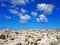 Rugged rocky arid limestone pavement landscape with vegetation in the cracks and blue sunlit sky with white clouds