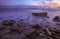 A rugged and rocky seascape at sunrise with waves flowing over harsh granite rocks.