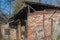 Ruined red-brick house with a low-slung verandah among tall, dry grass stalks and bare trees with signs of fire, blackened roof