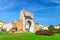 Ruins of ancient brick wall and stone gate Arch of Augustus Arco di Augusto, green lawn with bush of flowers in Rimini