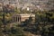 Ruins of ancient Greek temple surrounded by park or forest. Old building with columns with modern city, urban background