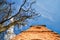 Ruins of an old abandoned church bell tower made of stone and a dry tree under a blue sky on a sunny day